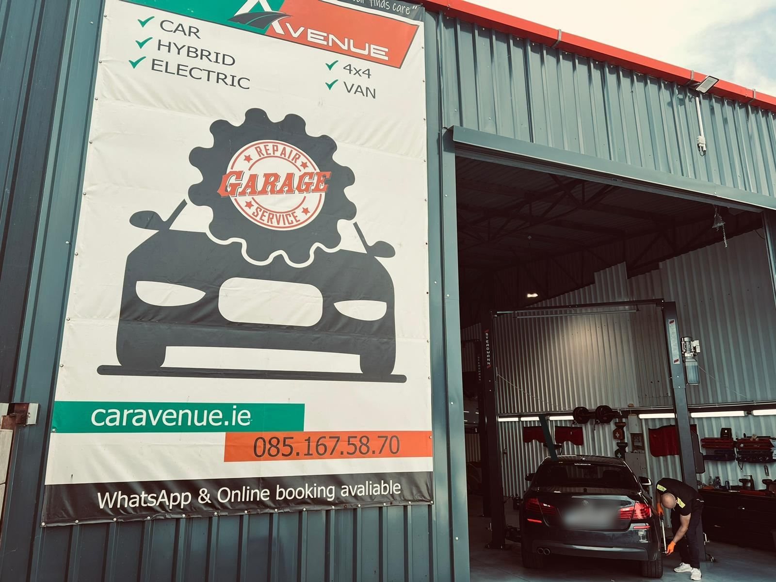 Car Avenue garage exterior with a large repair service banner and open bay where a mechanic works on a car