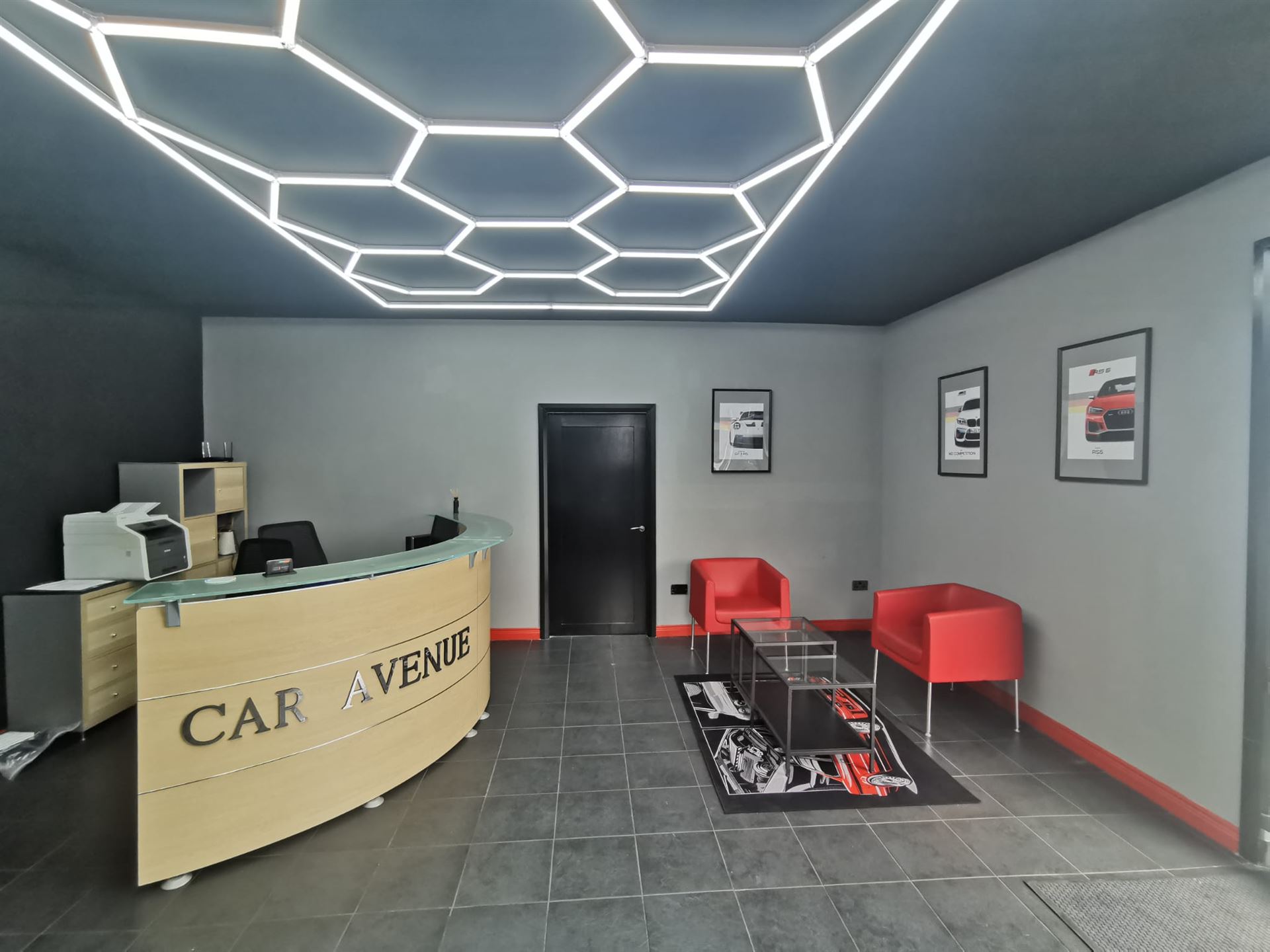 Auto garage reception and waiting area with a front desk, red chairs and hexagonal ceiling lights