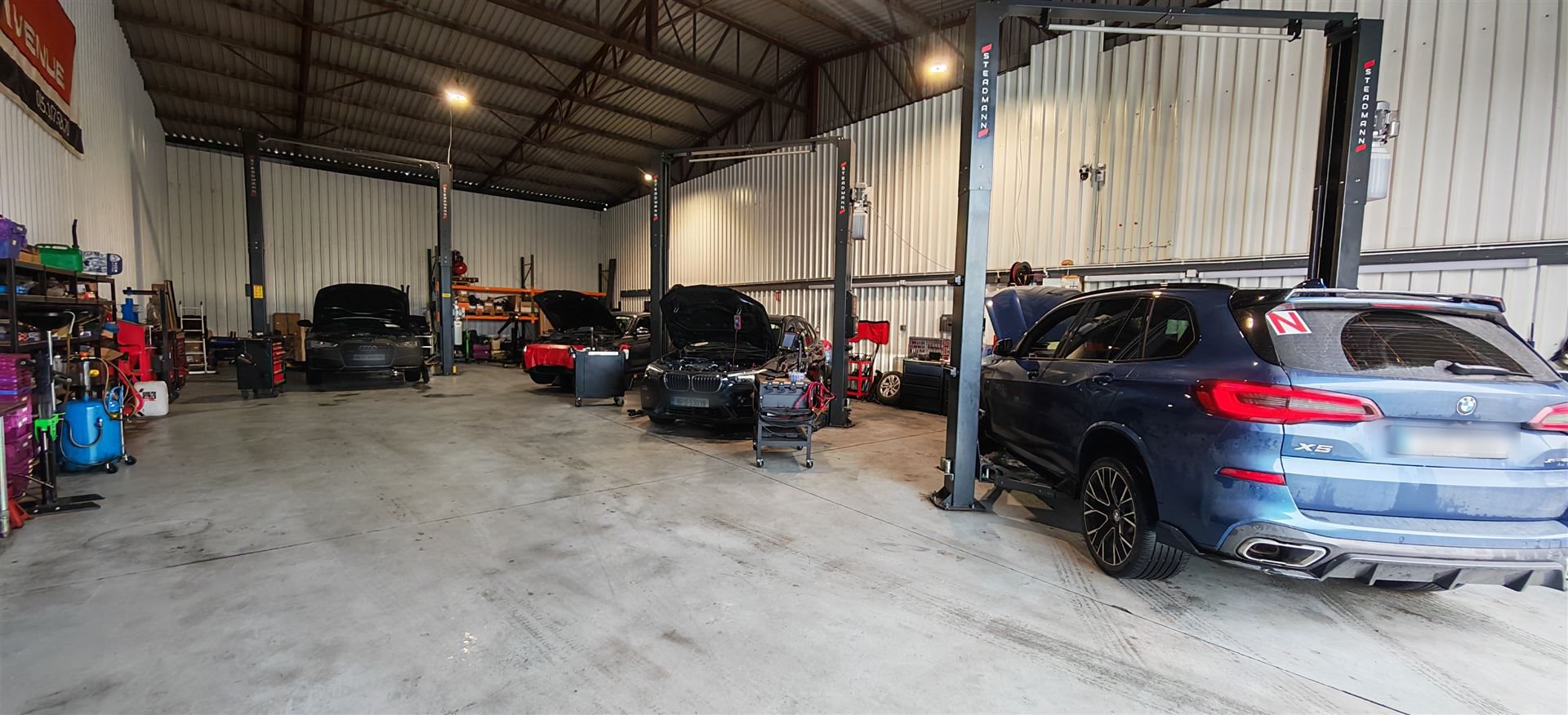Wide view of an auto repair workshop with several cars, two-post lifts and a blue BMW X5 in the service bay