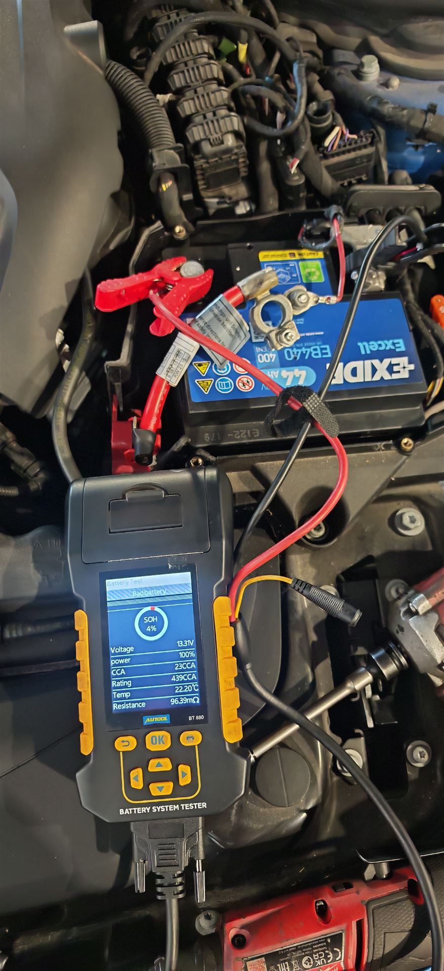 Digital battery system tester connected to a car battery under the hood to check battery health