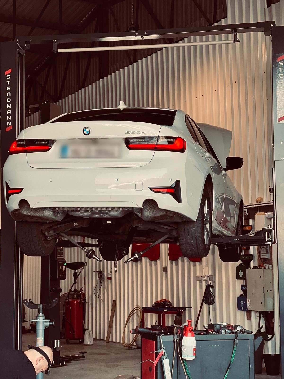White BMW sedan raised on a two-post lift for service inside an auto repair garage