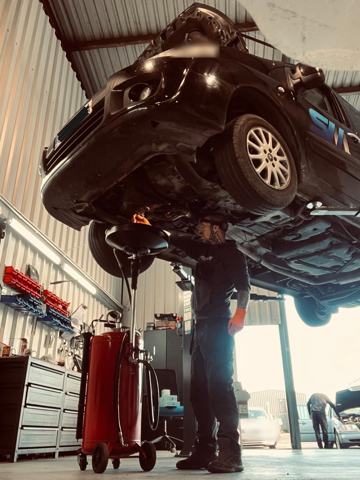 Mechanic performing an oil change on a car raised on a lift in an auto repair garage